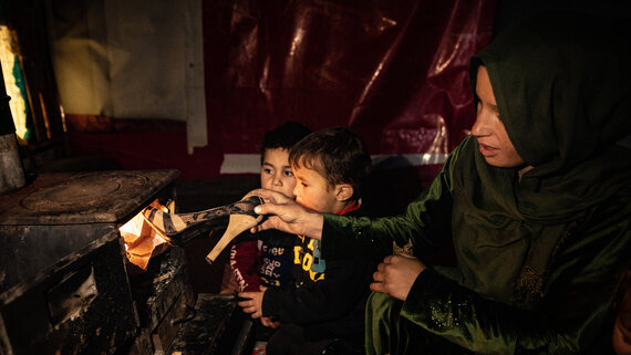 Refugee woman Manal, is putting a broken woman shoe into the stove to light the fire and heat the tent to keep warm